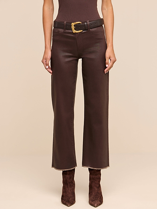 A person wearing the Wanda Coated Cropped Wide-Leg Jean with a black belt and brown suede boots, standing against a beige background.