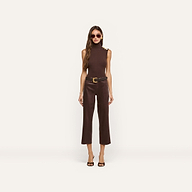 A woman stands against a plain white background wearing a sleeveless dark java brown top with gold buttons, the Wanda Coated Cropped Wide-Leg Jean in brown, a black belt with a gold buckle, sunglasses, and heeled sandals.