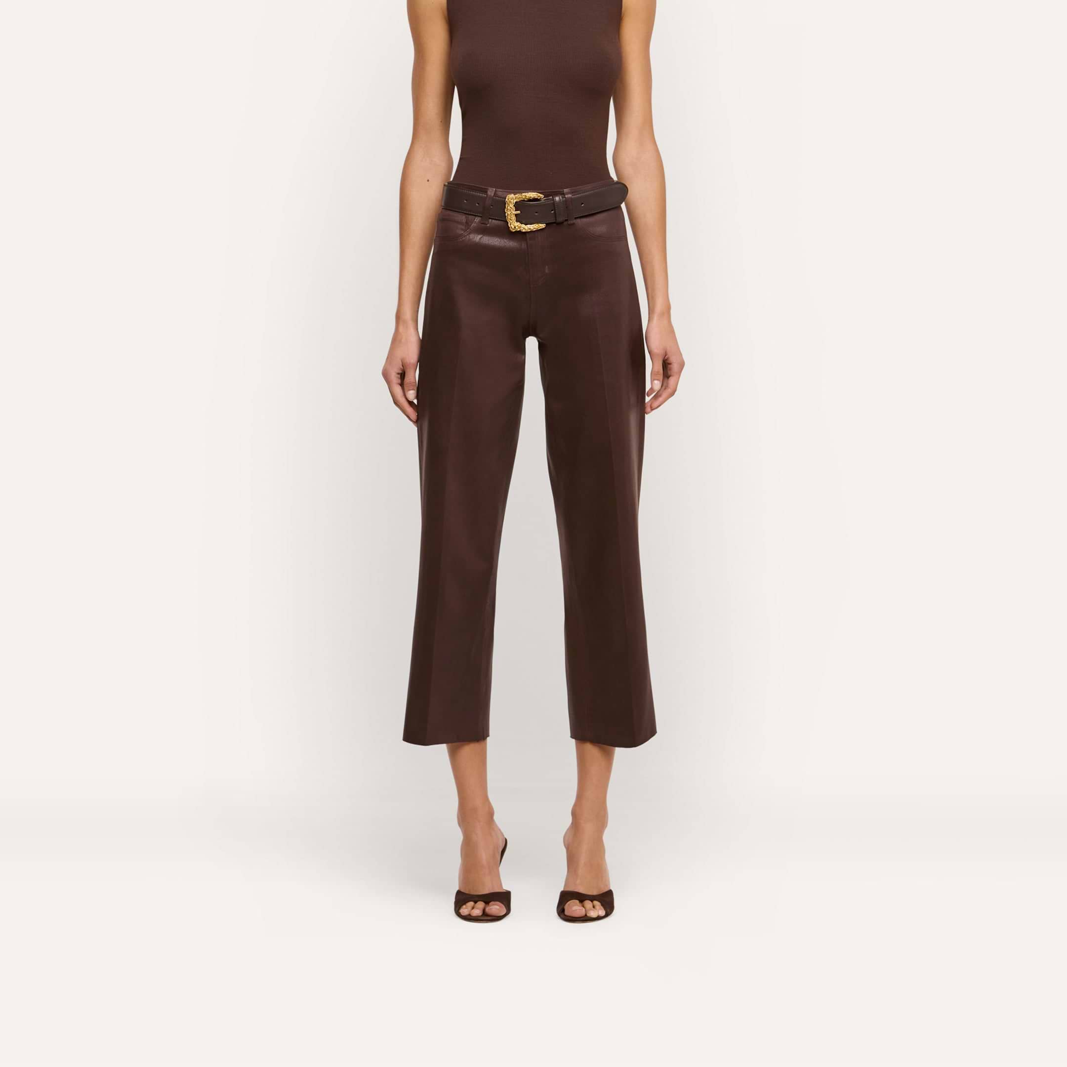 A woman stands against a plain white background wearing a sleeveless dark java brown top, open-toed heels, and the Wanda Coated Cropped Wide-Leg Jean with a wide belt.