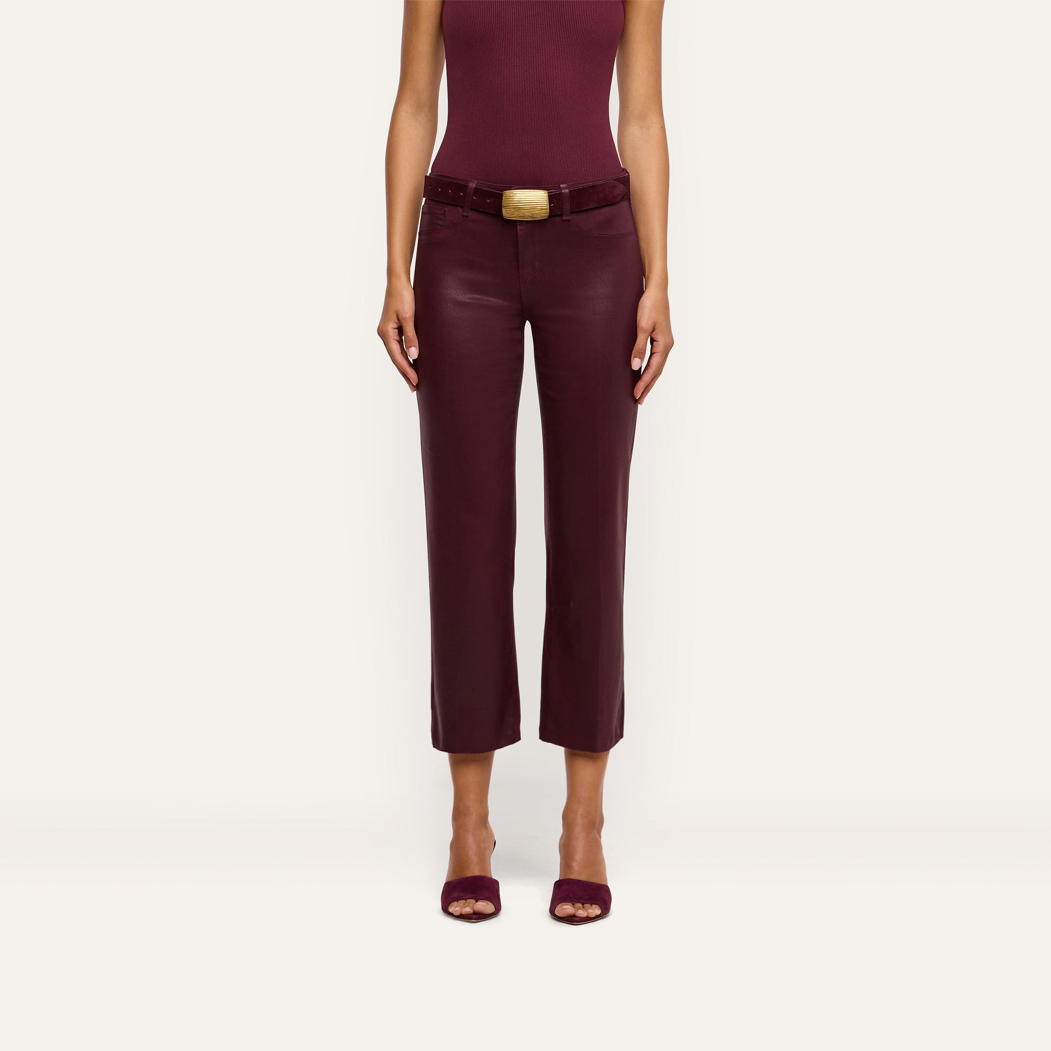 A woman is wearing the Wanda Coated Cropped Wide-Leg Jean, paired with a sleeveless burgundy top and open-toed shoes, standing against a plain light background. Her head is not visible in the image.
