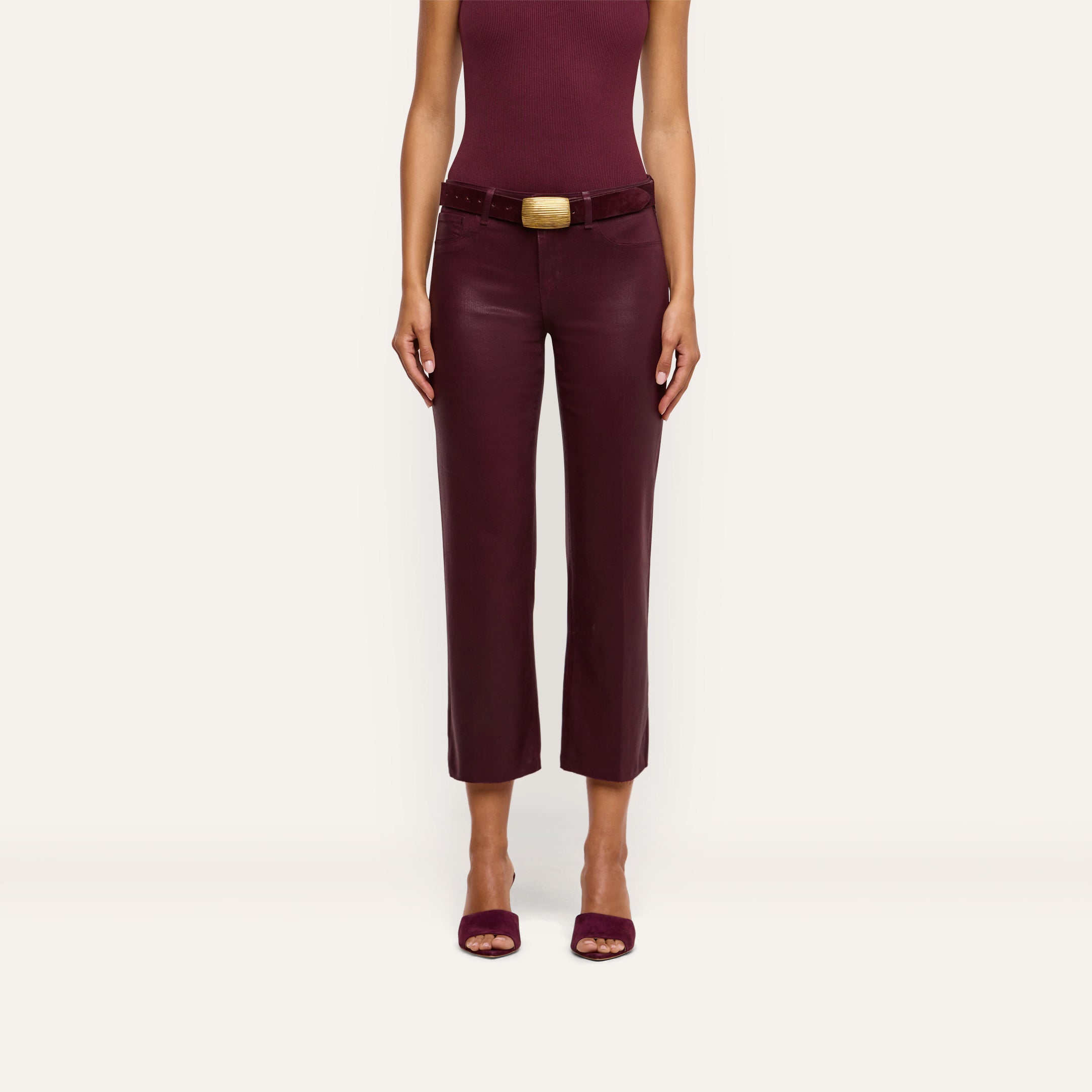A woman is wearing the Wanda Coated Cropped Wide-Leg Jean, paired with a sleeveless burgundy top and open-toed shoes, standing against a plain light background. Her head is not visible in the image.