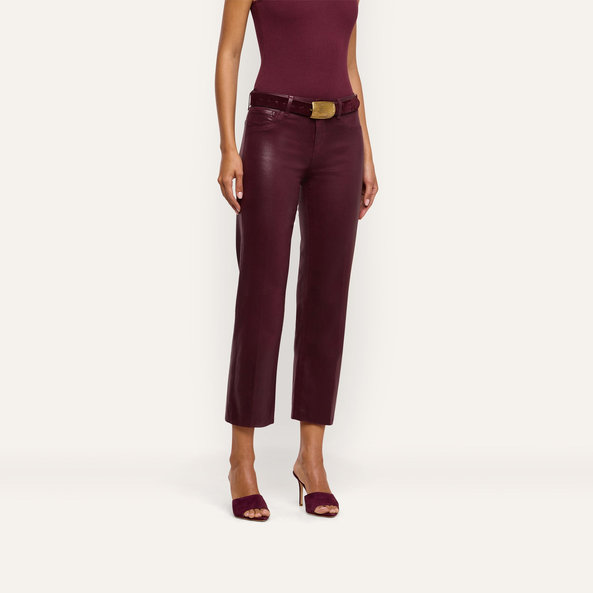 A woman is shown from shoulders to feet wearing a sleeveless burgundy top, open-toe heeled sandals, and the Wanda Coated Cropped Wide-Leg Jean in a high-rise burgundy style with a belt.