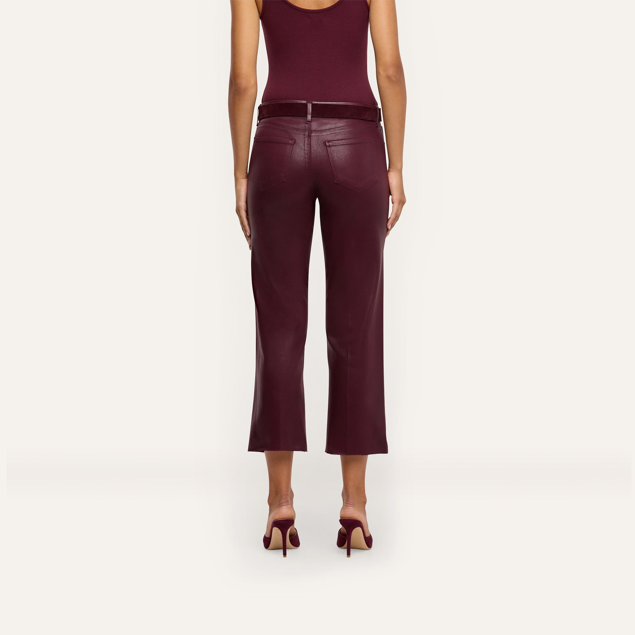 A woman is shown from the back, standing against a plain light background, wearing a sleeveless burgundy top, matching high heels, and the Wanda Coated Cropped Wide-Leg Jean in burgundy.