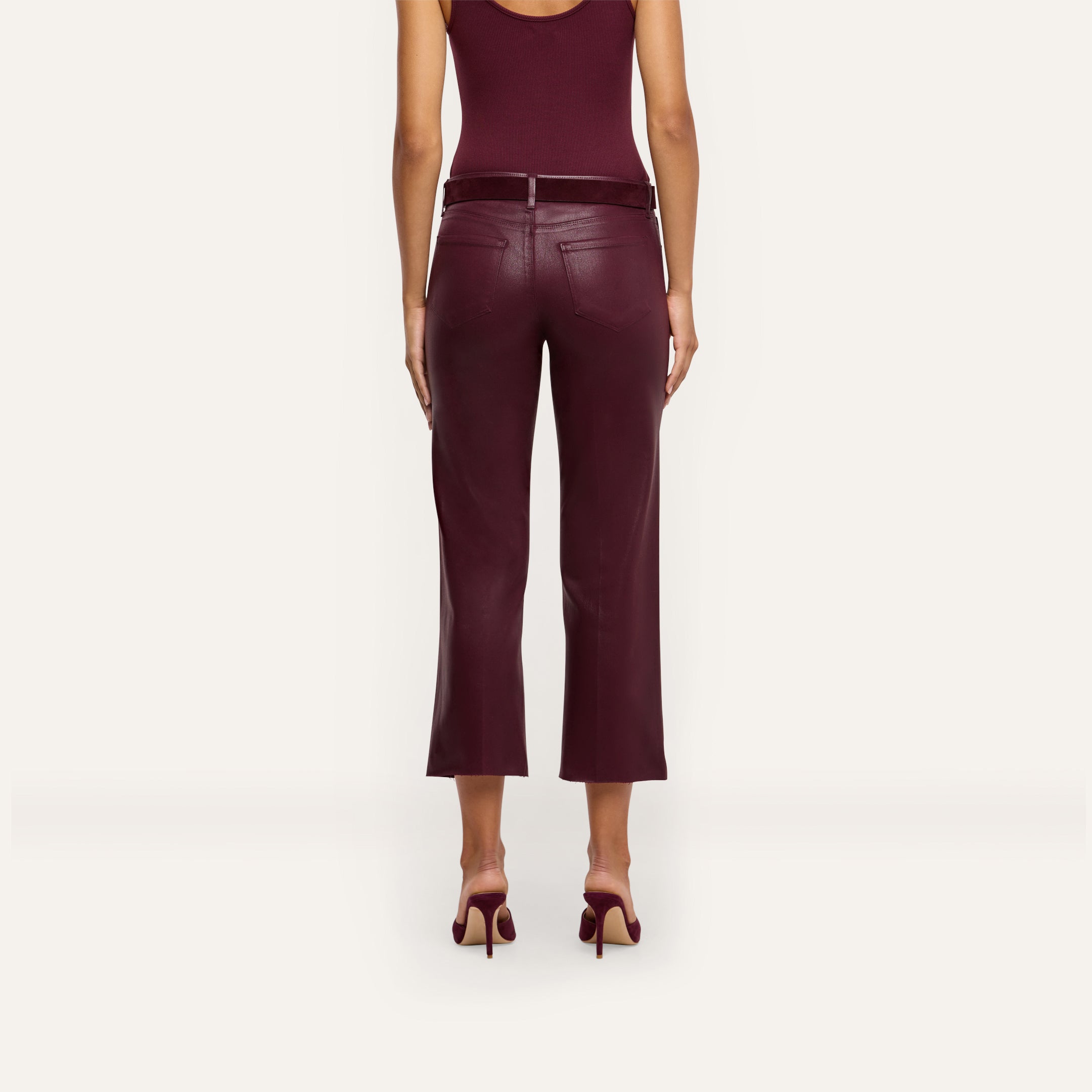 A woman is shown from the back, standing against a plain light background, wearing a sleeveless burgundy top, matching high heels, and the Wanda Coated Cropped Wide-Leg Jean in burgundy.