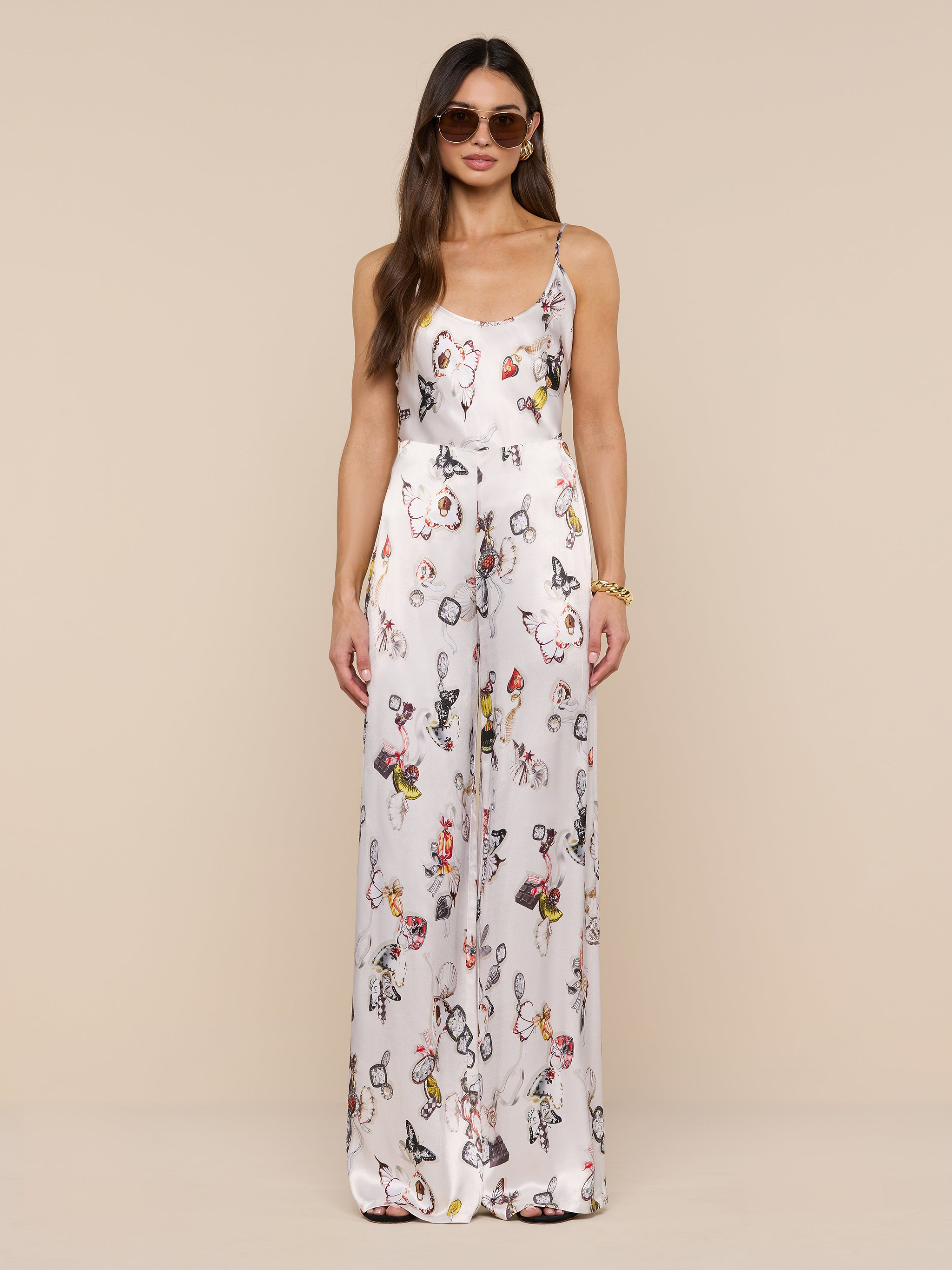 A woman in sunglasses wears the Kimia Satin Pant—a white, high-rise, straight-leg style—paired with a sleeveless floral top, standing against a plain white background and facing forward with her hands by her sides.