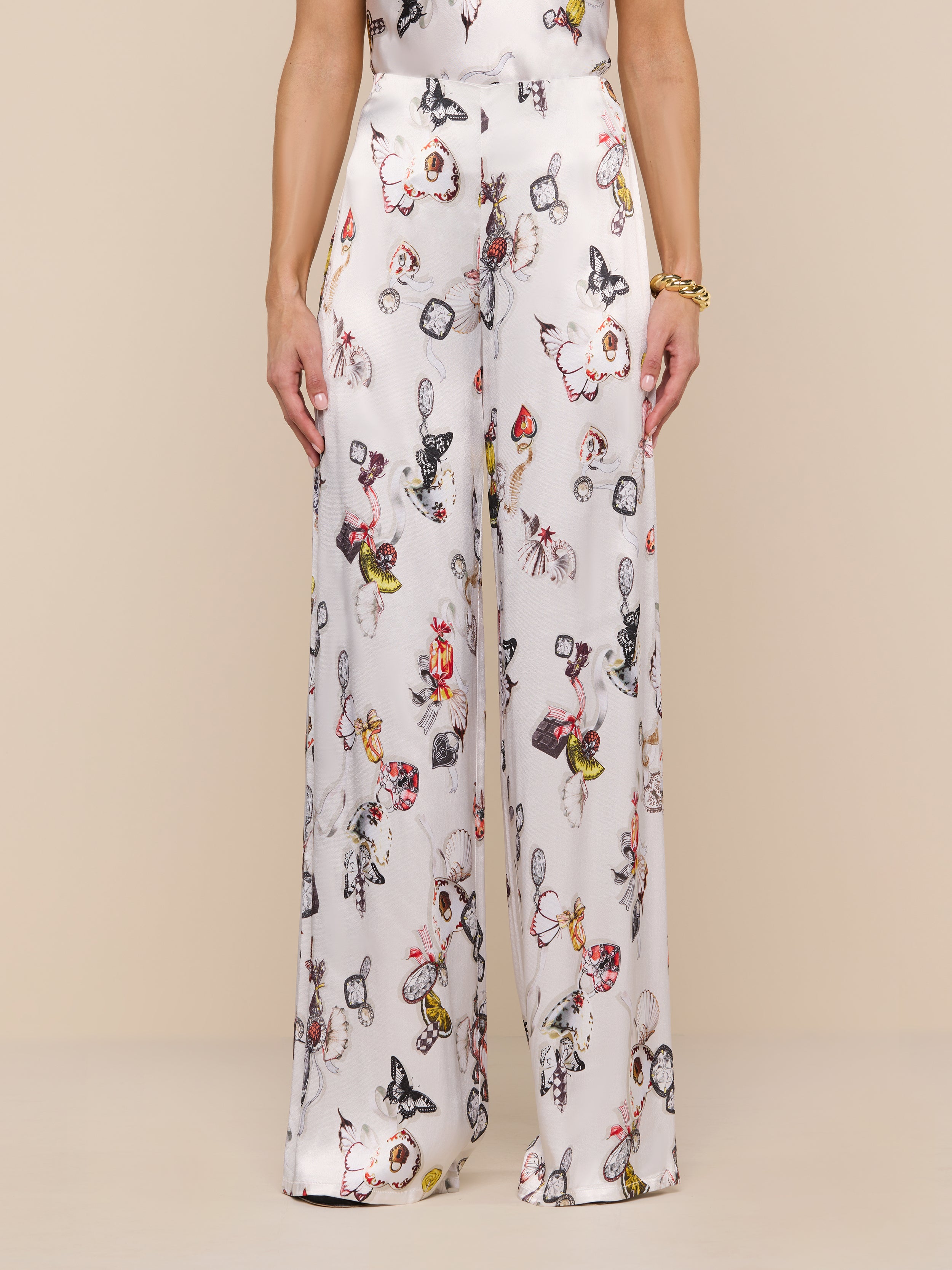A person, shown from the lower torso down, stands against a plain white background wearing the Kimia Satin Pant—a high-rise, wide-leg style featuring a colorful butterfly print.