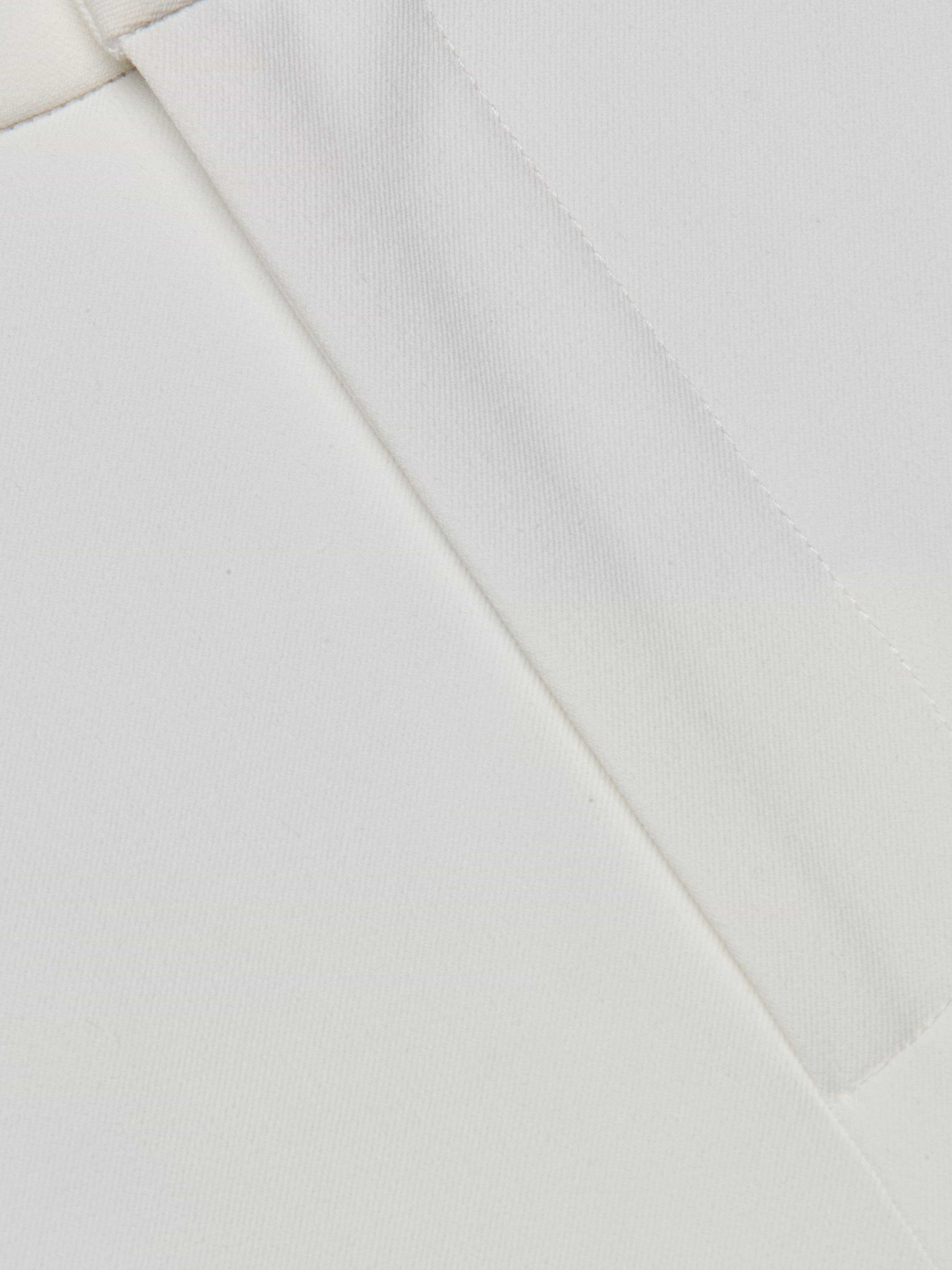 Close-up of the Rebel Trouser white stretch fabric, featuring two seams intersecting at an angle to showcase the texture and detailed stitching.