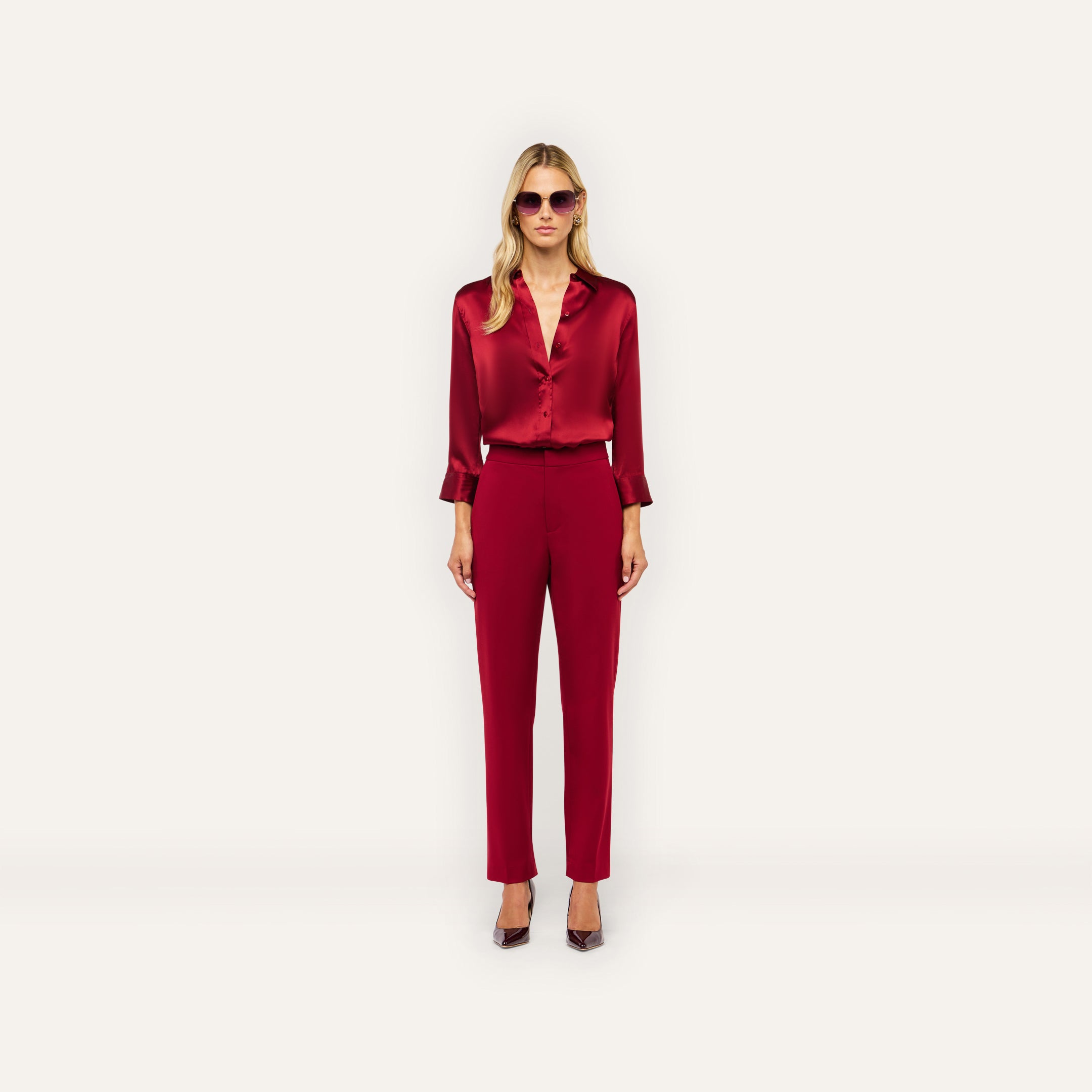 A woman wears a long-sleeved burgundy button-down shirt tucked into matching high-rise slim-straight Rebel Trousers and dark heels.