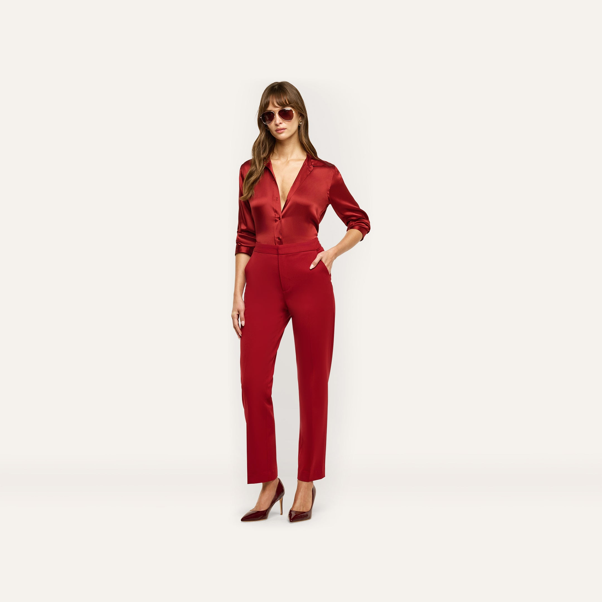 A woman wears a deep red tailored button-down shirt with matching Rebel Trouser high-waisted slim-straight trousers and pointed-toe heels.