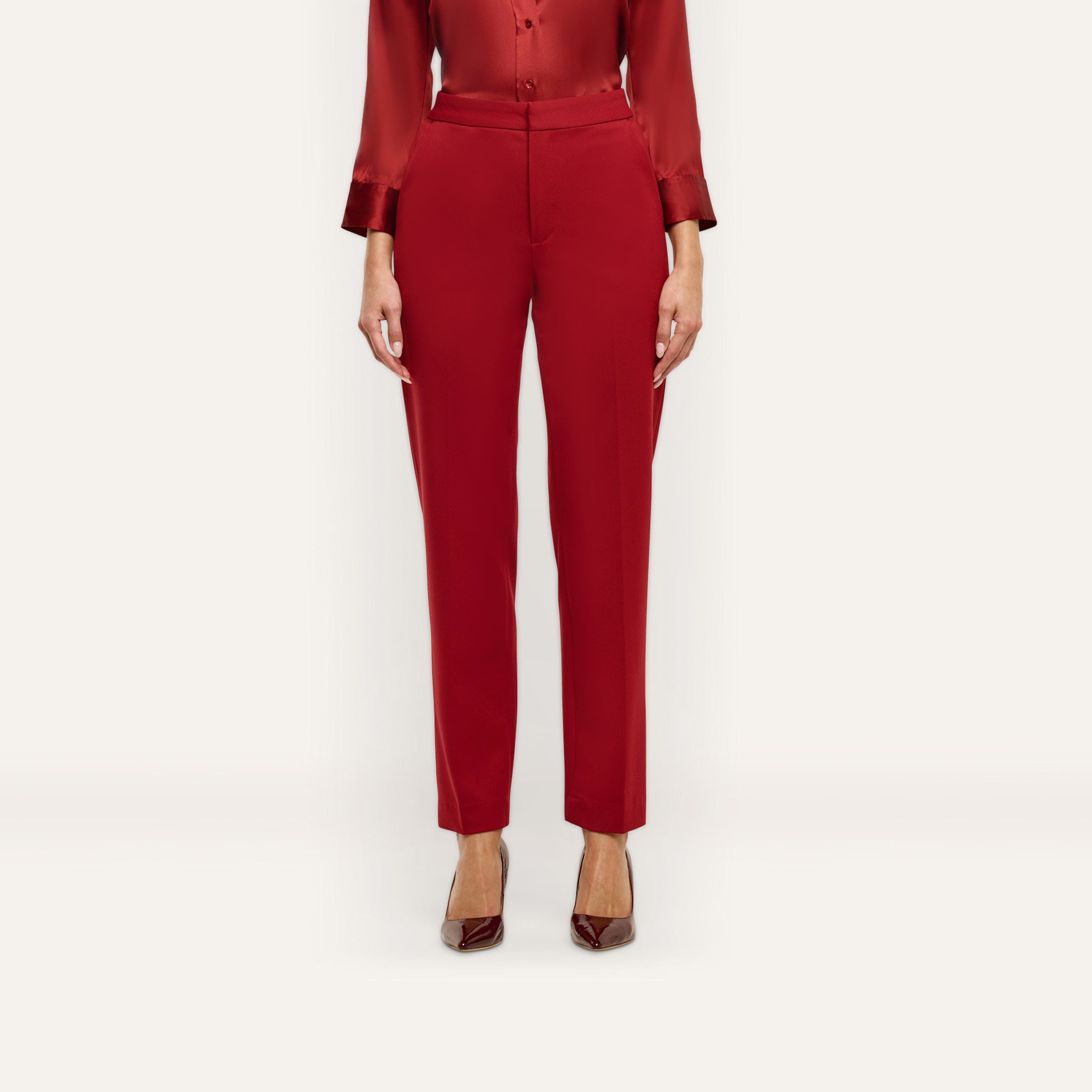 A person wearing Rebel Trouser high-waisted, slim-straight red stretch twill trousers, a matching red long-sleeved button-up shirt, and dark pointed-toe heels.