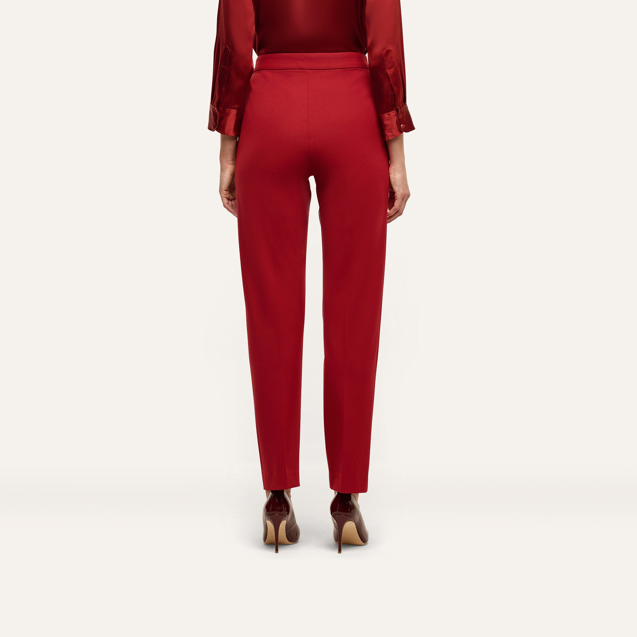 Back view of red Rebel Trouser high-waisted, slim-straight trousers paired with a red button-down shirt and pointed-toe heels in tailored statement stretch twill.