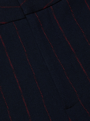 Close-up of the Rebel Pinstriped Trouser by L'AGENCE, featuring dark navy blue twill fabric with thin vertical red pinstripes, visible seam, and waistband detail.