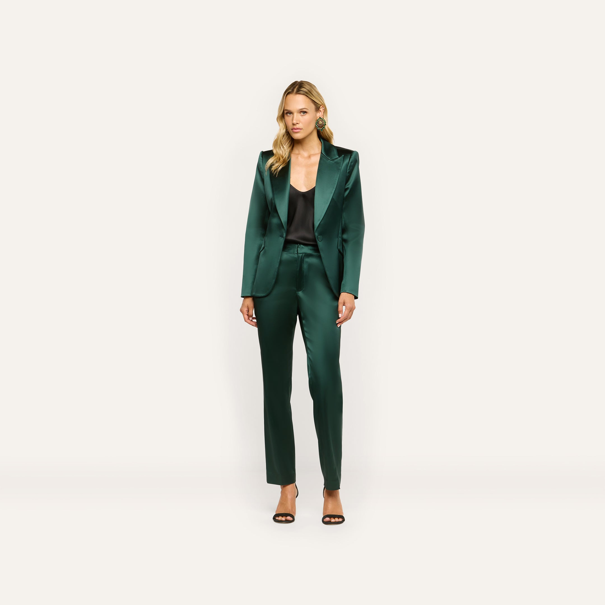 A woman wearing a dark green satin blazer and Rebel Satin Trouser over a black camisole, finished with black heeled sandals for a tailored statement.