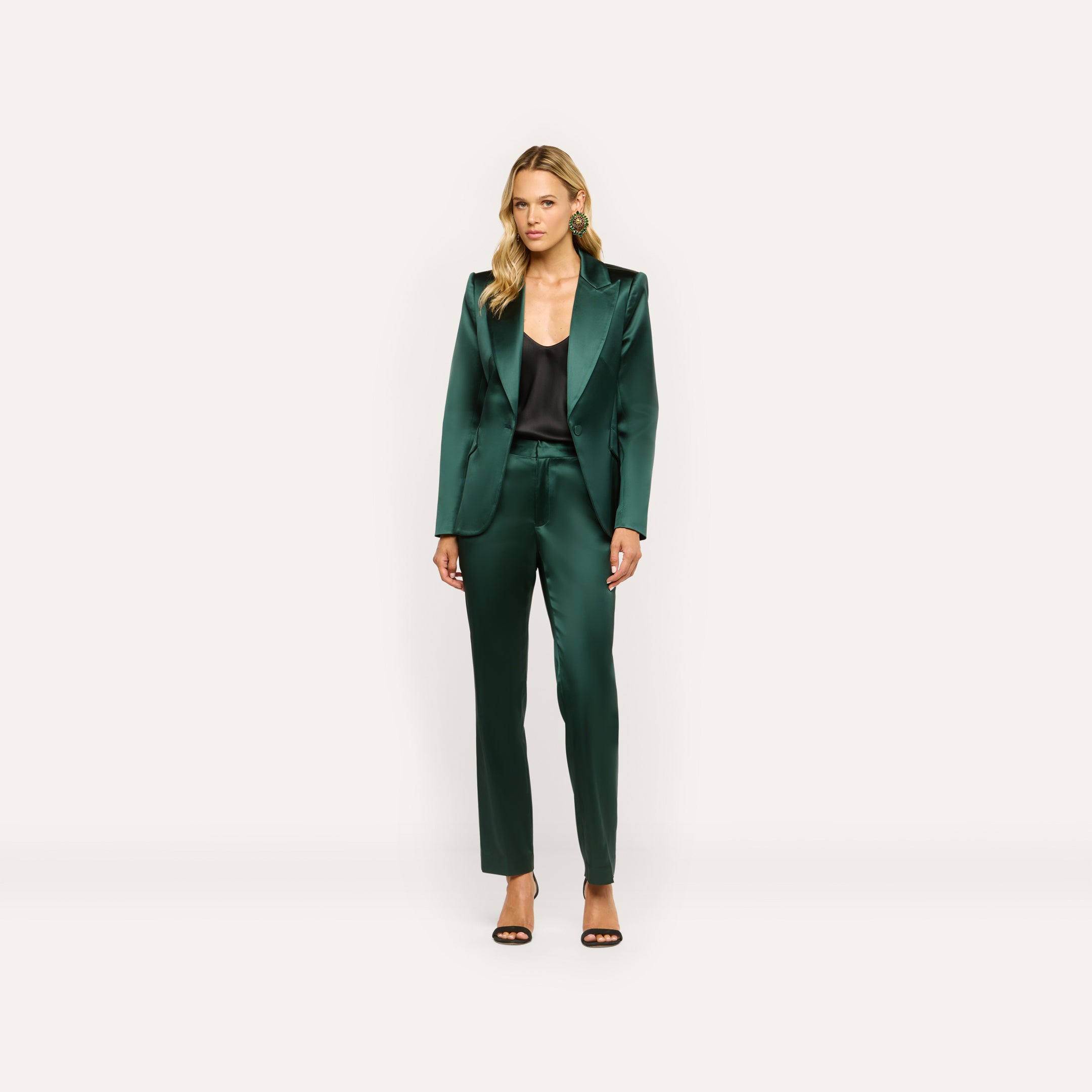 A woman wearing a dark green satin blazer and Rebel Satin Trouser over a black camisole, finished with black heeled sandals for a tailored statement.