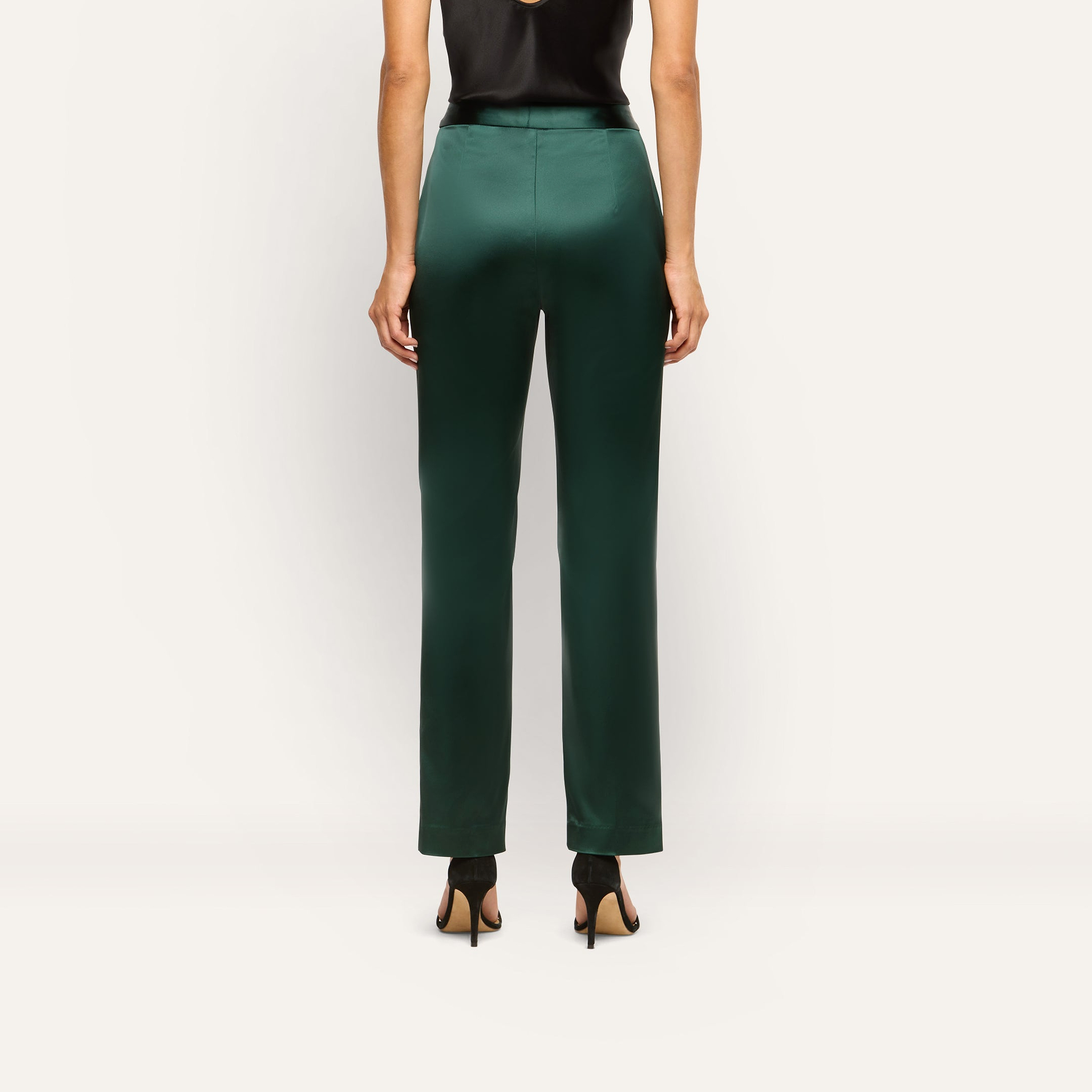 Back view of a person wearing dark green slim-straight Rebel Satin Trousers and black high-heeled sandals.