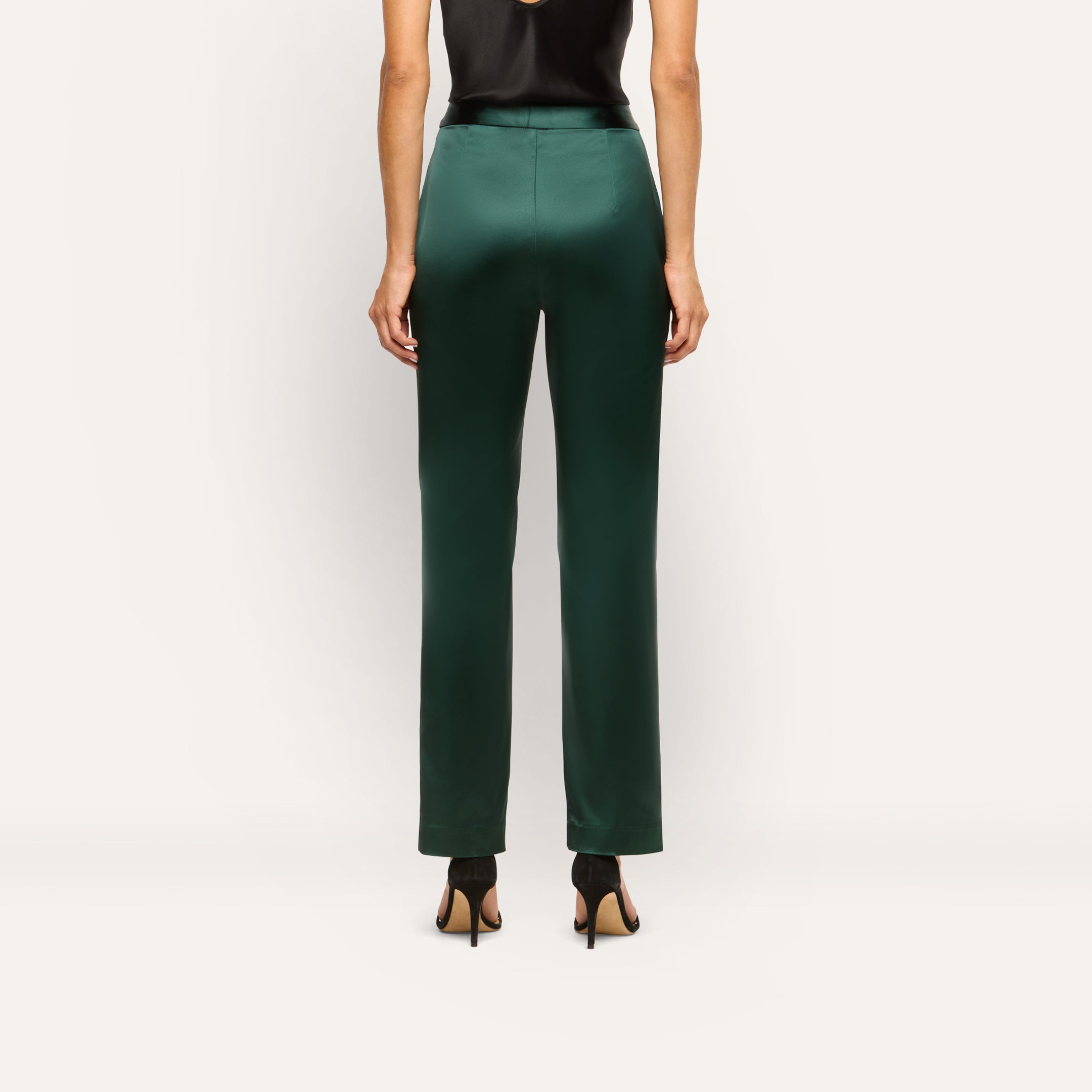 Back view of a person wearing dark green slim-straight Rebel Satin Trousers and black high-heeled sandals.