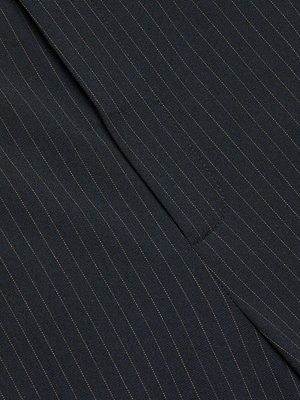 Close-up of dark fabric with thin, navy pinstripes, featuring a seam and flap—details from the Rebel Pinstriped Trouser.