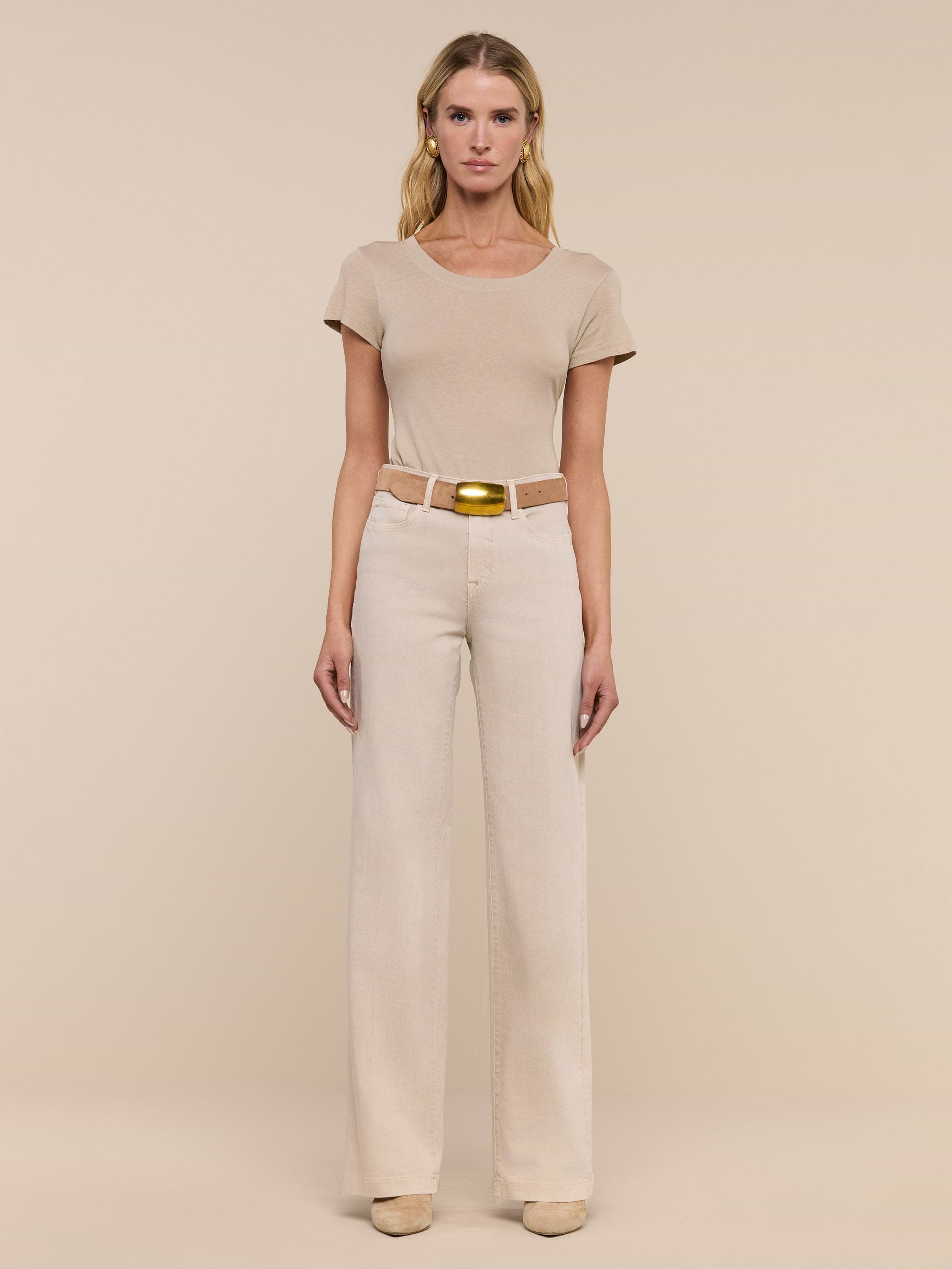 A woman stands facing forward in a beige short-sleeve top, the Clayton Wide-Leg Jean in stretch denim with a belt, and beige shoes, against a plain white background.