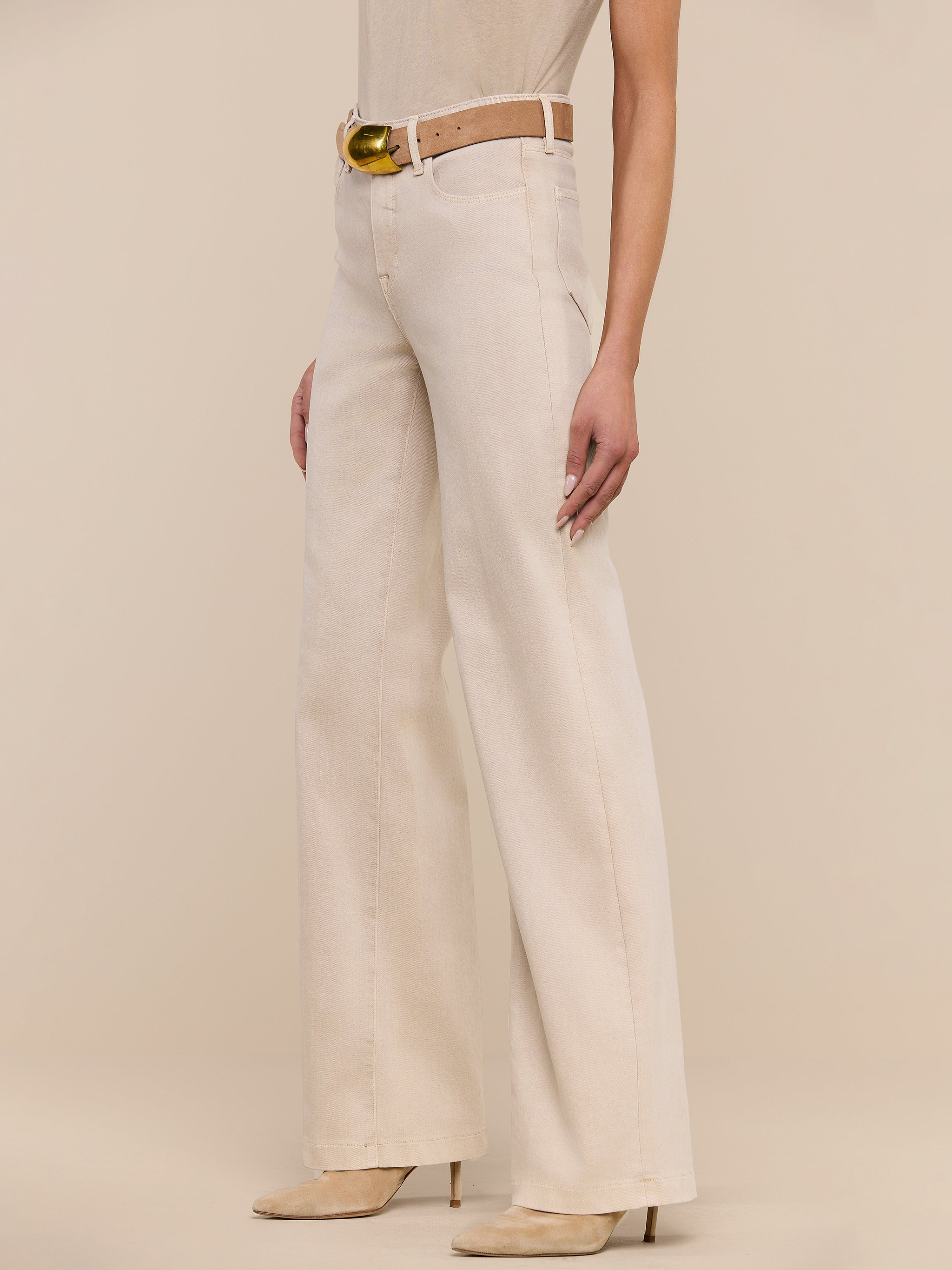 Model showcases the Clayton Wide-Leg Jean with its high-waisted fit, matching belt, and heeled shoes, standing against a plain white background. Only the lower half of the body is visible.