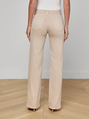 Someone is shown from the back wearing Clayton Wide-Leg Jeans in beige high rise with a white sleeveless top, standing on a light wooden floor against a plain light-colored wall.