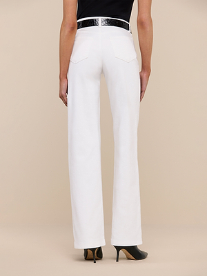 Someone is seen from behind, modeling the Clayton Wide-Leg Jean—high-waisted, white stretch denim pants—styled with a black belt and black high-heeled shoes, against a plain beige background.