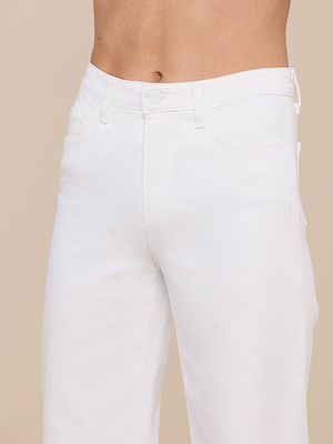 A close-up of a person wearing the Clayton Wide-Leg Jean in white stretch denim, showcasing the waist and upper thigh. This high-rise style features five-pocket construction, belt loops, and a button closure against a beige background.