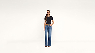 A woman in a black t-shirt, blue flared jeans, a brown belt, and sunglasses.