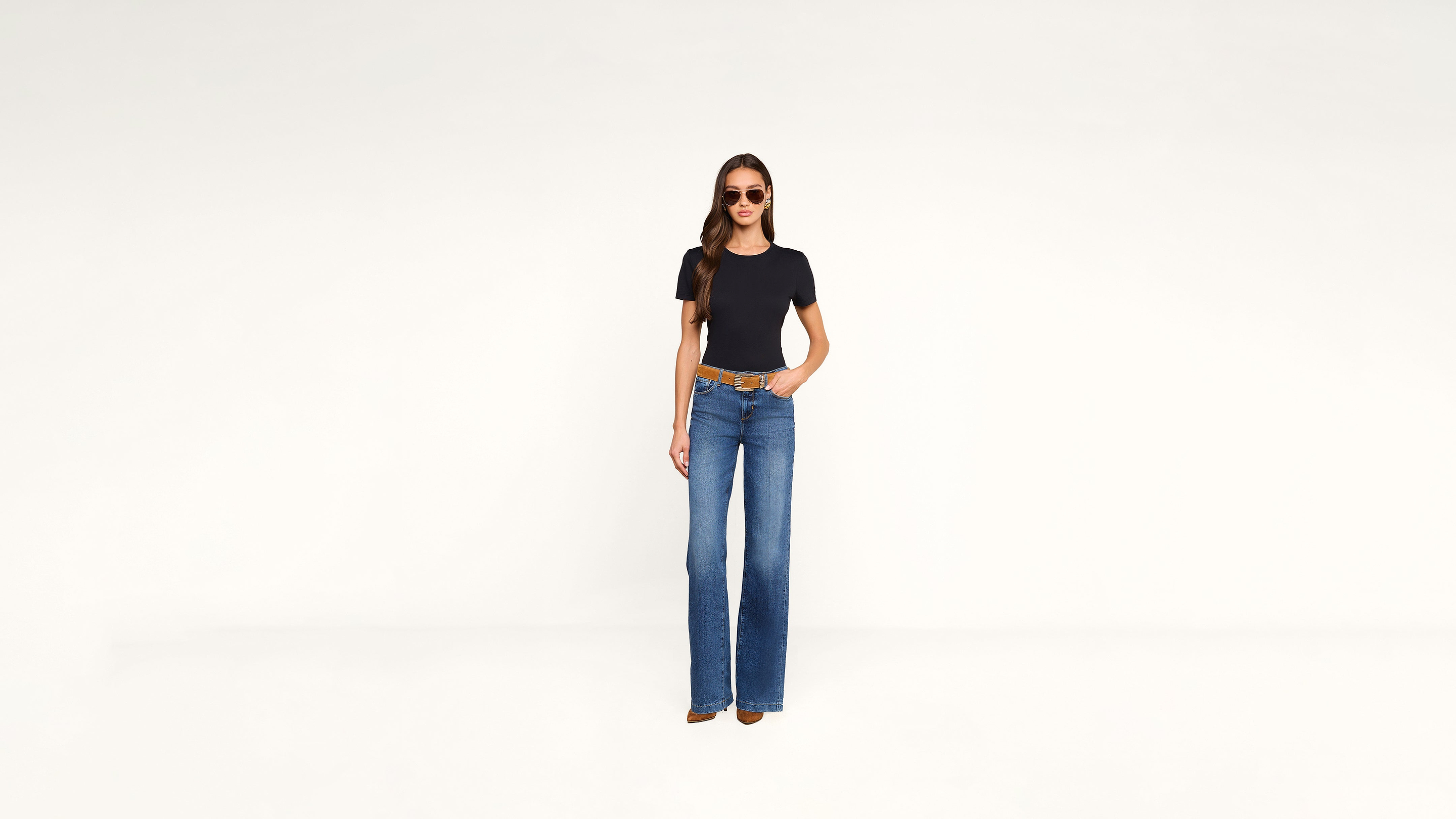 A woman in a black t-shirt, blue flared jeans, a brown belt, and sunglasses.