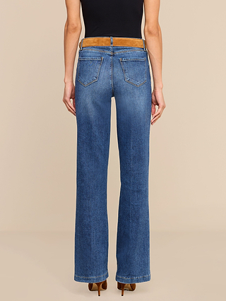 A person wearing Clayton Wide-Leg Jeans in blue with back pockets and a brown suede waistband, standing against a beige background.