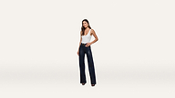 A woman stands facing forward, wearing a white sleeveless top and high-waisted dark flared pants with black heels, styled with a modern and minimalist touch against a plain white background.