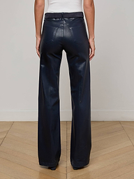 A person stands on a wooden floor, back to the camera, showcasing the L'AGENCE Clayton Coated Wide-Leg Jean in dark navy with a sleeveless white top.