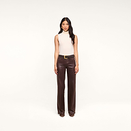 A woman stands facing forward against a plain white background, wearing a sleeveless beige top, brown shoes, and the Clayton Coated Wide-Leg Jean—dark brown high-rise coated denim pants with a belt.