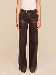 A person is standing against a plain white background, wearing a sleeveless beige top, the Clayton Coated Wide-Leg Jean in dark brown with a black belt, and brown pointed shoes.