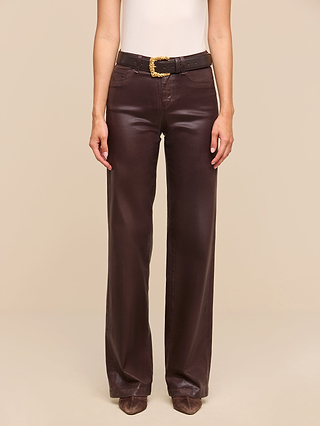 A person wearing the Clayton Coated Wide-Leg Jean in dark brown with a black belt featuring a gold buckle, a white sleeveless top, and brown pointed-toe shoes stands against a beige background.