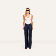 A woman wearing sunglasses, a white tank top, black belt, and Clayton Coated Wide-Leg Jean stands facing forward against a plain light background.