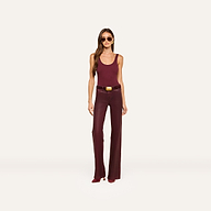 A woman wearing sunglasses, a sleeveless maroon top, the Clayton Coated Wide-Leg Jean with a contoured waistband and belt in dark maroon, and maroon heeled shoes, stands against a plain light background.