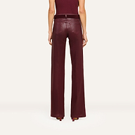 A person stands facing away, wearing the Clayton Coated Wide-Leg Jean featuring a contoured waistband in a rich burgundy hue, paired with a matching belt and heels. The background is plain and light-colored.