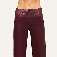 A person wearing high-waisted, shiny burgundy leather pants stands against a plain light background, with the image cropped to show only the waist and upper legs.