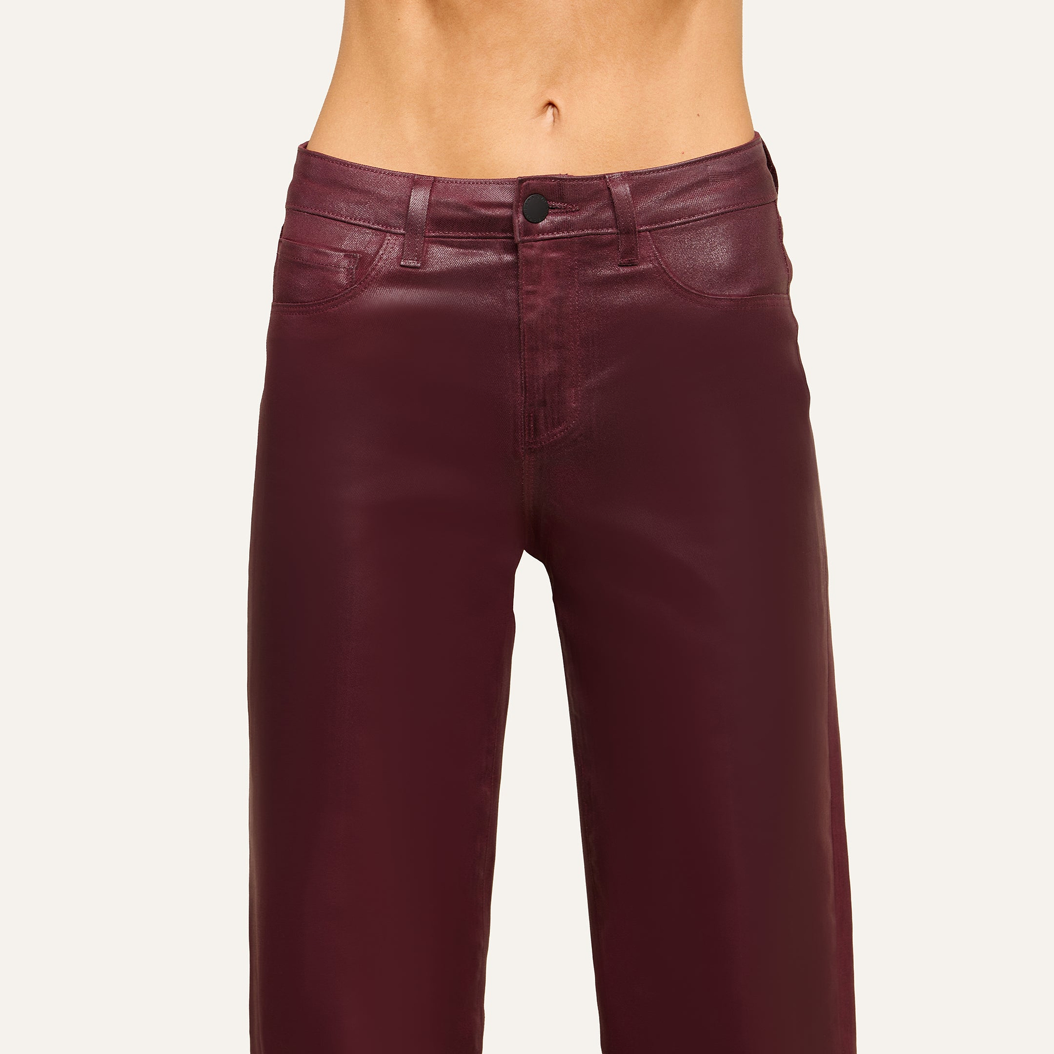 A person wearing high-waisted, shiny burgundy leather pants stands against a plain light background, with the image cropped to show only the waist and upper legs.