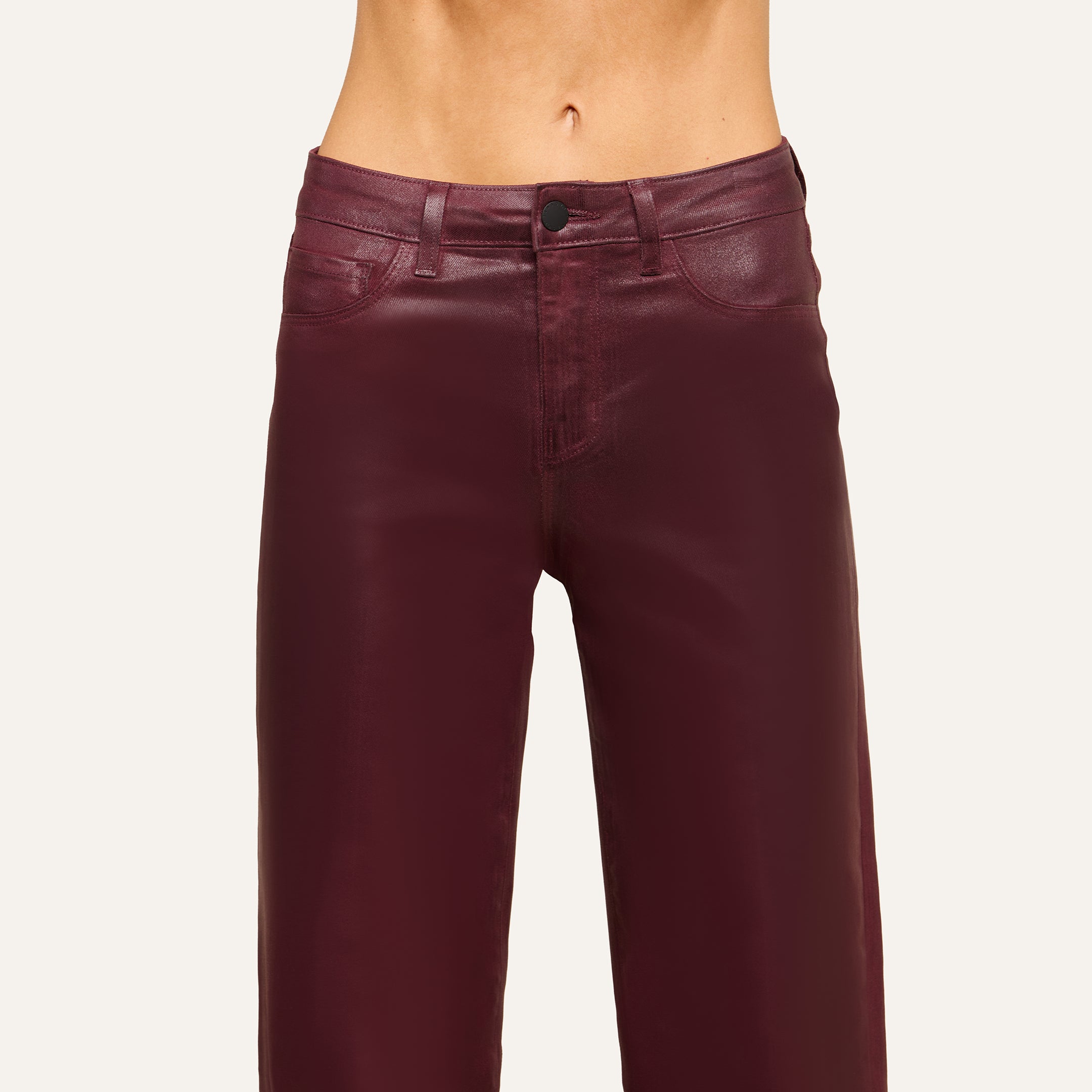 A person wearing high-waisted, shiny burgundy leather pants stands against a plain light background, with the image cropped to show only the waist and upper legs.