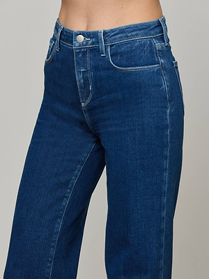 A close-up photo of a person wearing the Clayton Wide-Leg Jean in an indigo wash, featuring a high-rise fit with button and zipper closure, shown from waist to mid-thigh against a plain background.