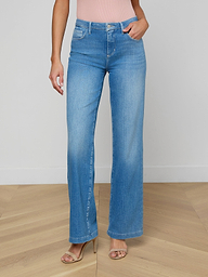 A person wearing the Clayton Wide-Leg Jean in light blue high-rise stretch denim, paired with a light pink sleeveless top and beige high-heeled sandals, stands against a plain white background.