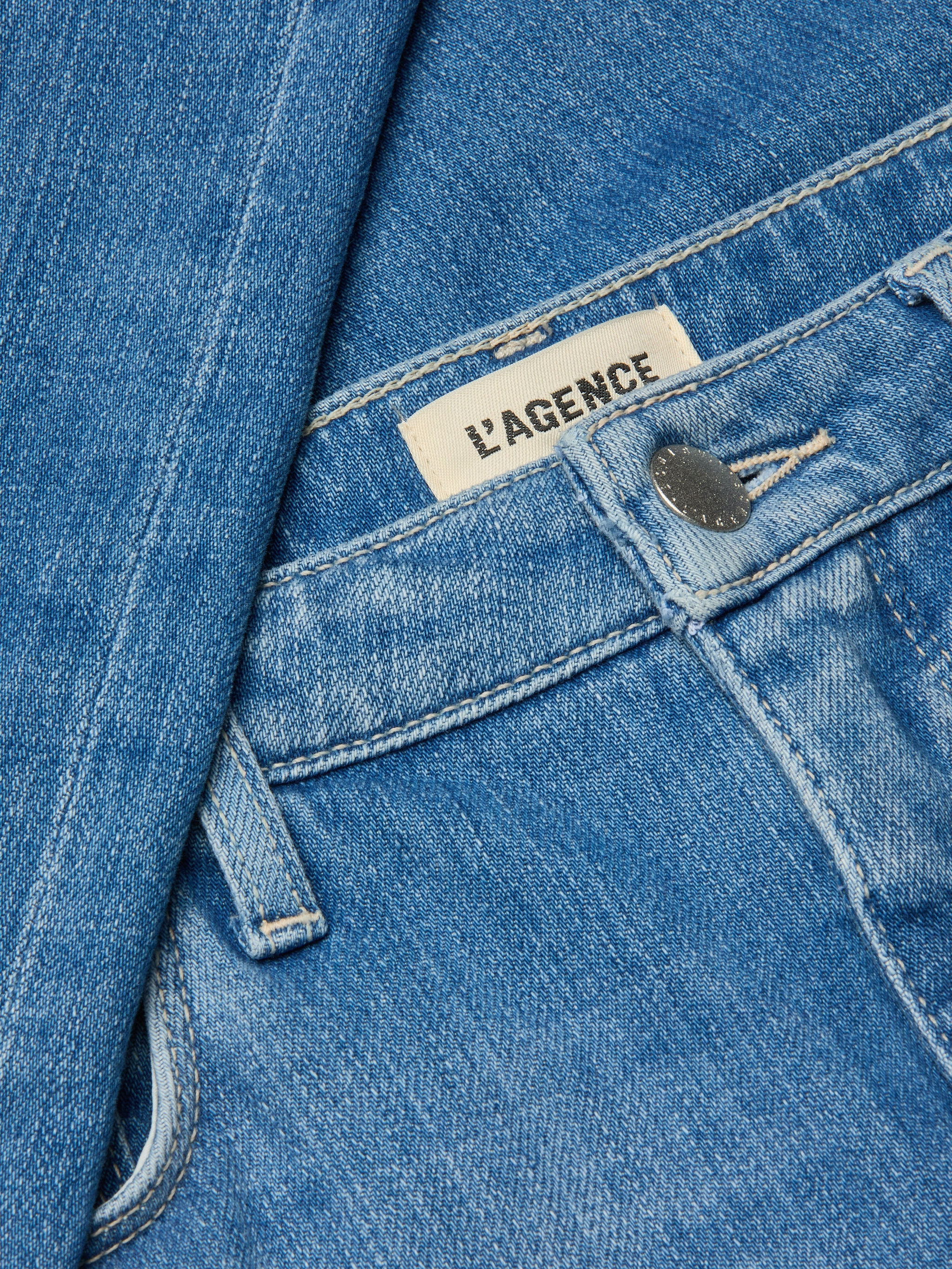 Close-up of the Clayton Wide-Leg Jean in blue denim, featuring a silver button, visible LAGENCE brand label, detailed stitching, and high rise stretch denim fabric.