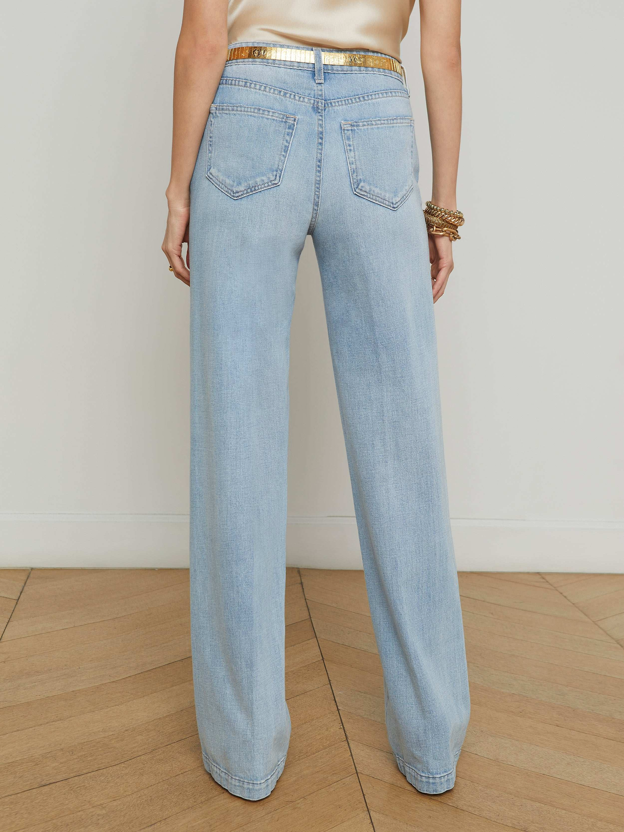 A person shown from the back with their hands by their sides, wearing the Clayton Wide-Leg Jean in a light wash and a gold belt, against a plain white background.