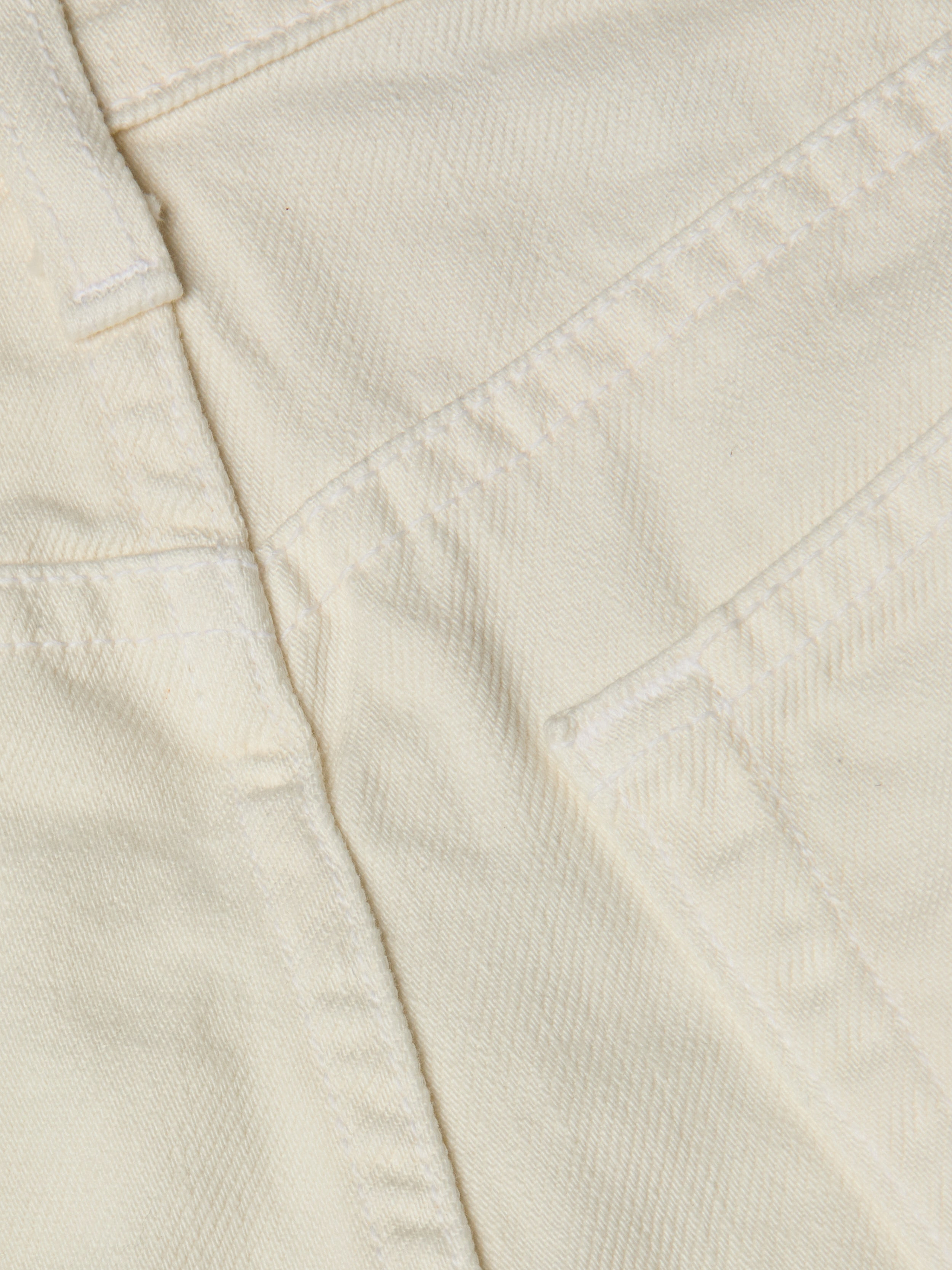 Close-up of cream-colored all-cotton denim fabric showing stitching, a seam, and part of the Clark Distressed Jean Short pocket.