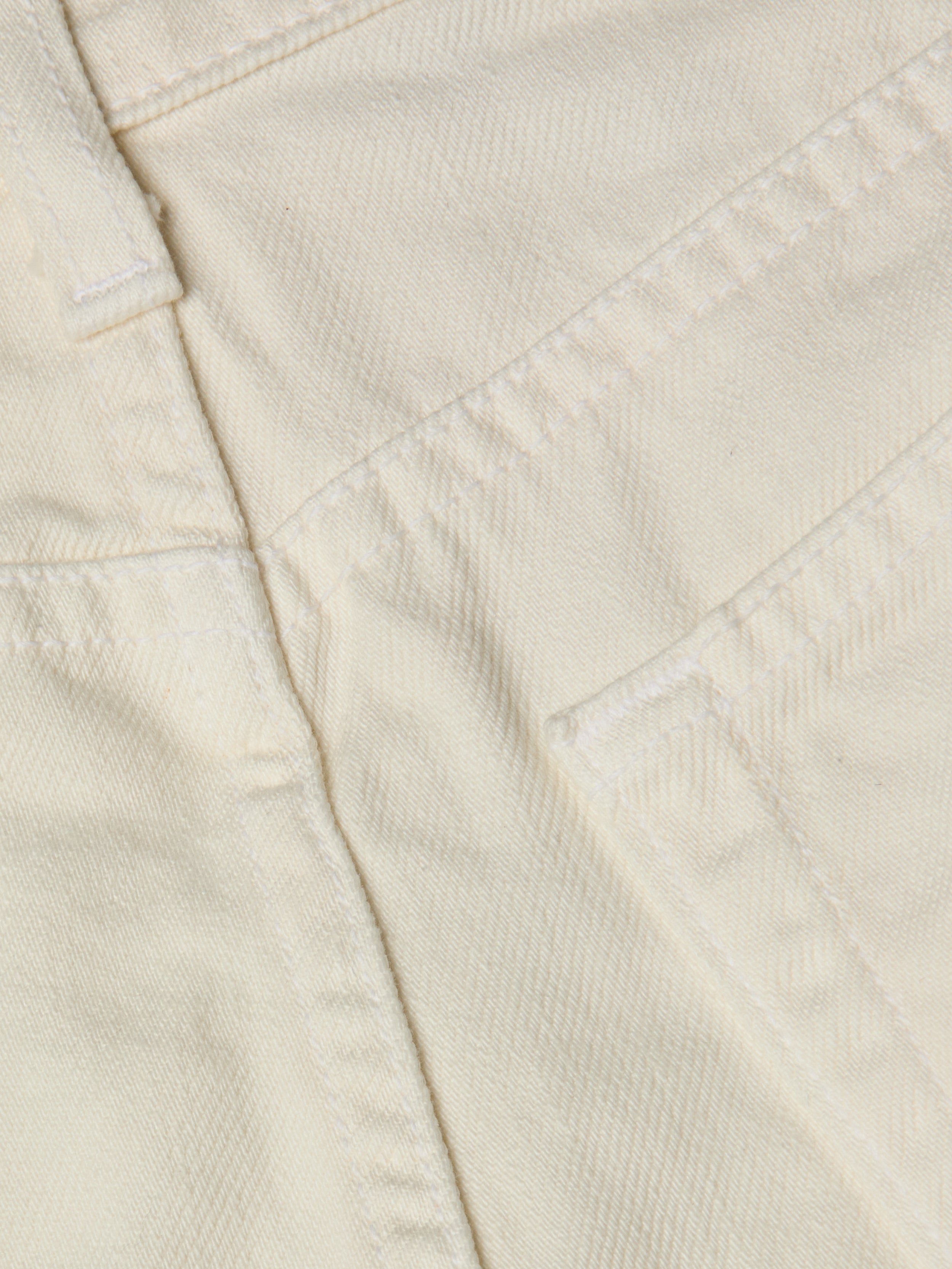 Close-up of cream-colored all-cotton denim fabric showing stitching, a seam, and part of the Clark Distressed Jean Short pocket.