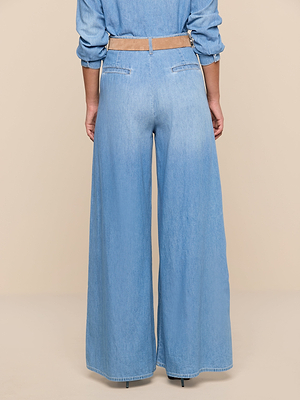 A person stands with their back to the camera, wearing the Lorenza Palazzo Jean, a matching denim shirt with rolled sleeves, a beige belt, and black shoes.