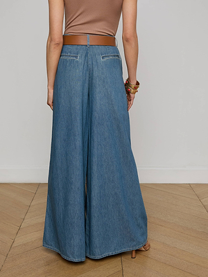 A person stands on a wooden floor, seen from behind, wearing a brown sleeveless top, a brown belt, bracelets, and the Lorenza Palazzo Jean in a vintage wash.