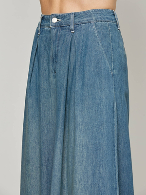 A close-up side view of a person wearing the Lorenza Palazzo Jean, a high-waisted, blue denim maxi skirt with pleats and waistband button closure, crafted from featherweight chambray in a vintage wash.
