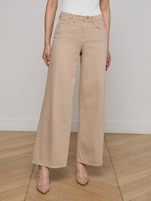 A person wearing the Alicent Wide-Leg Jean by L'AGENCE Sale in beige and pointed nude heels stands on a wooden floor against a plain white wall, with their upper body partially out of frame.